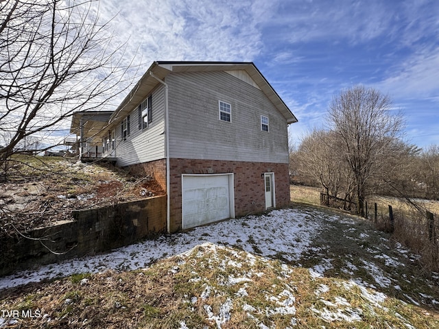 view of snowy exterior featuring a garage and brick siding