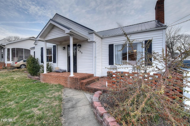 view of front of house with metal roof, a front lawn, a chimney, and a sunroom