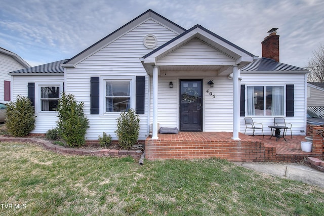 bungalow with a standing seam roof, metal roof, covered porch, a chimney, and a front yard