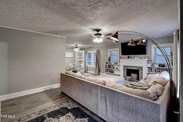 living room featuring plenty of natural light, crown molding, a stone fireplace, and wood finished floors