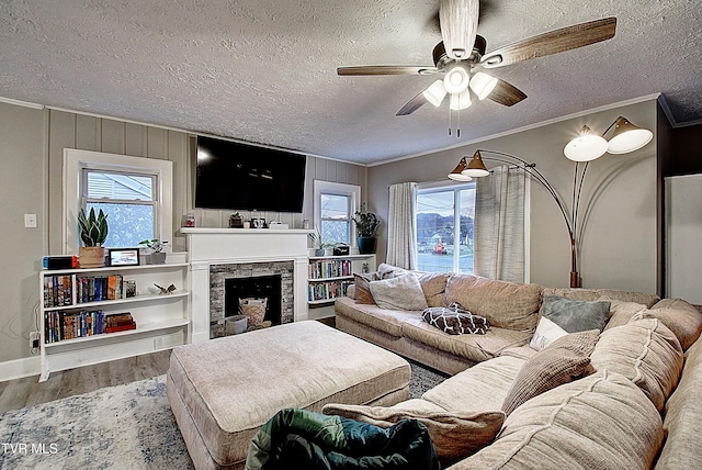 living area featuring a fireplace, crown molding, a ceiling fan, a textured ceiling, and wood finished floors