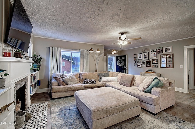 living room with ceiling fan, a fireplace with flush hearth, wood finished floors, baseboards, and ornamental molding