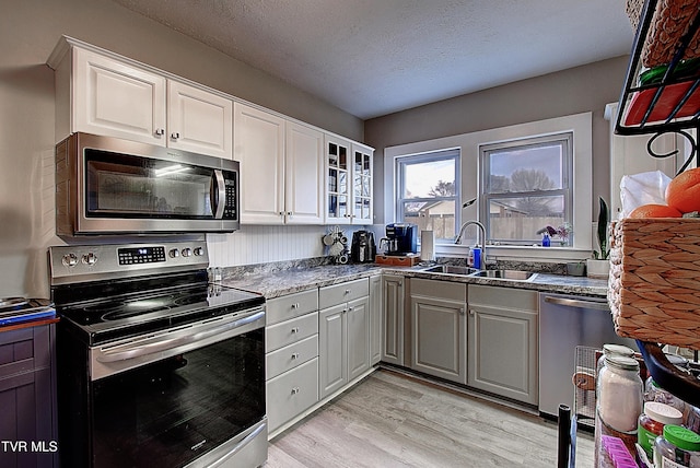 kitchen featuring stainless steel appliances, light wood-style flooring, glass insert cabinets, a sink, and a textured ceiling