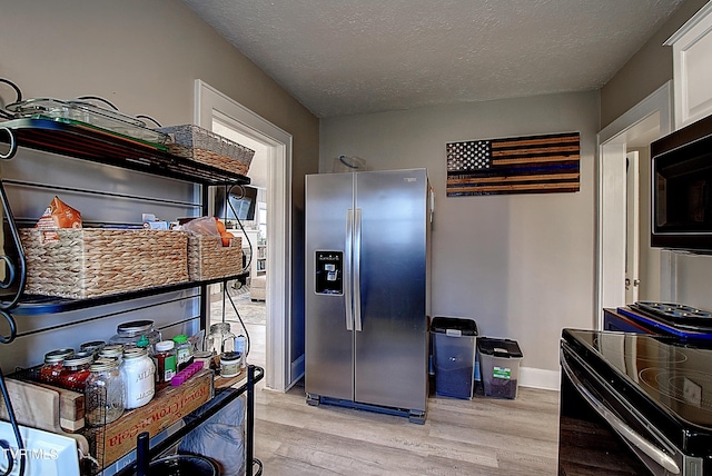 kitchen with a textured ceiling, black range with electric cooktop, white cabinetry, light wood-style floors, and stainless steel fridge