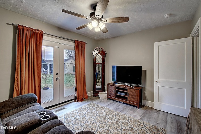 living area with a textured ceiling, ceiling fan, visible vents, french doors, and light wood finished floors