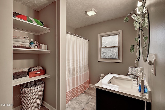 full bath featuring a textured ceiling, baseboards, wood finished floors, and vanity