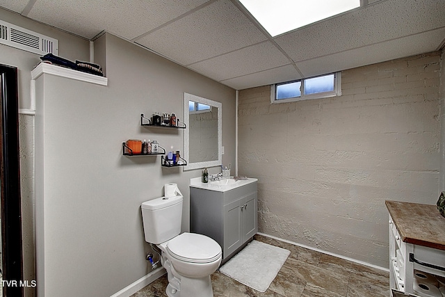 bathroom featuring baseboards, a drop ceiling, toilet, stone finish flooring, and vanity