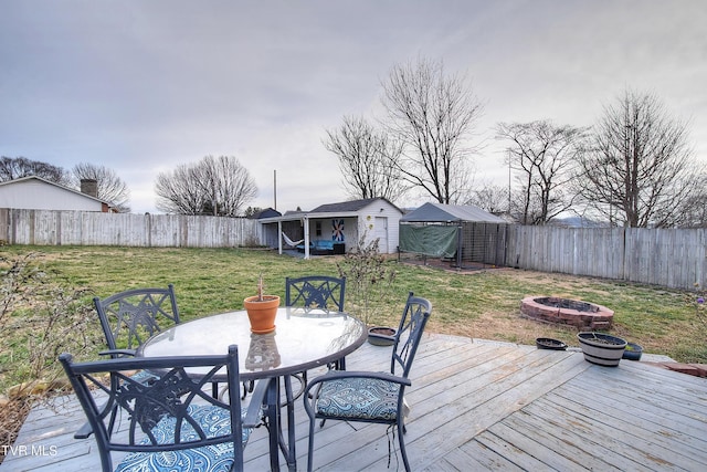 wooden terrace with an outbuilding, an outdoor fire pit, a fenced backyard, a yard, and outdoor dining space