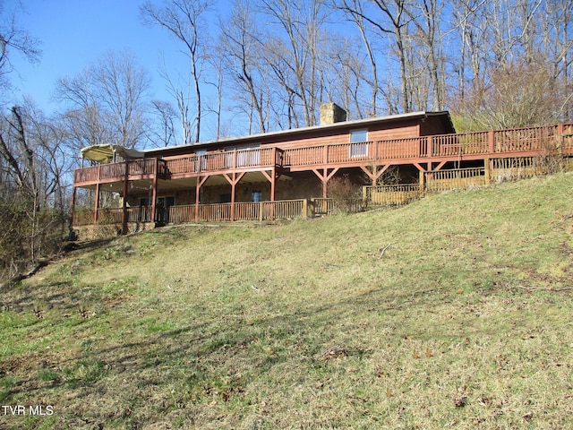 rear view of property featuring a chimney, a lawn, and a deck