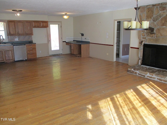 kitchen with brown cabinets, dark countertops, hanging light fixtures, stainless steel dishwasher, and a sink