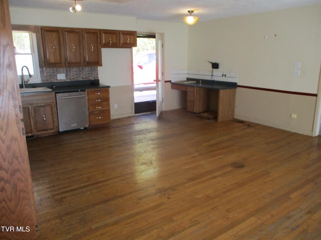 kitchen featuring dark wood-style flooring, a sink, brown cabinets, dishwasher, and dark countertops