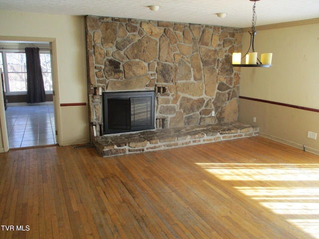 unfurnished living room with a textured ceiling, baseboards, wood finished floors, and a stone fireplace