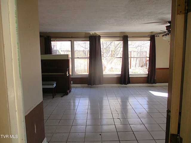 empty room featuring a textured ceiling, light tile patterned floors, and a ceiling fan