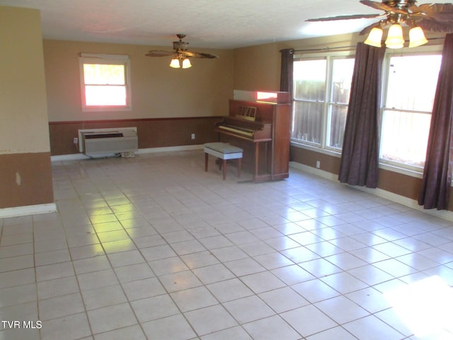 unfurnished living room with light tile patterned floors, ceiling fan, wainscoting, and plenty of natural light