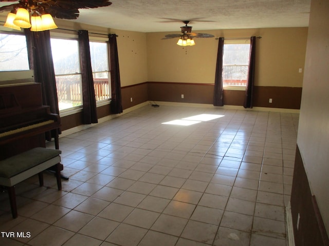 empty room featuring a textured ceiling, light tile patterned floors, a ceiling fan, and baseboards