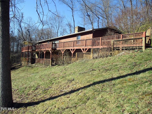 back of property featuring a deck, a lawn, and a chimney