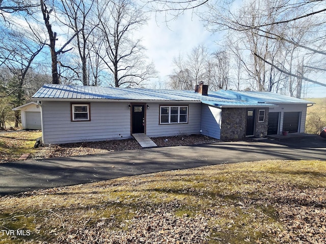 view of front of property with driveway, stone siding, metal roof, and a chimney