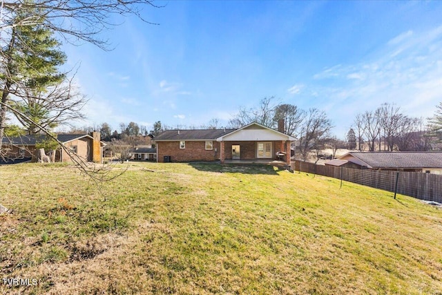 rear view of house featuring fence, a lawn, and brick siding