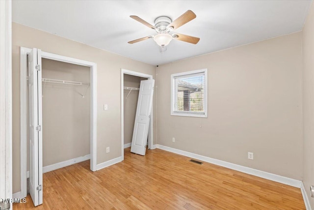 unfurnished bedroom featuring baseboards, visible vents, light wood finished floors, and two closets