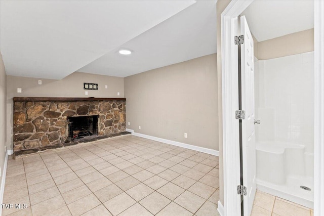 unfurnished living room with light tile patterned floors, baseboards, and a stone fireplace