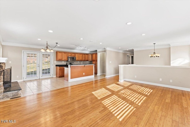 unfurnished living room with a chandelier, ornamental molding, and light wood-style floors