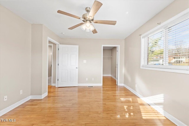 unfurnished bedroom with a ceiling fan, baseboards, a closet, light wood-type flooring, and a walk in closet