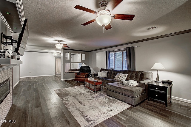 living area with visible vents, ornamental molding, a textured ceiling, dark wood-style floors, and a brick fireplace