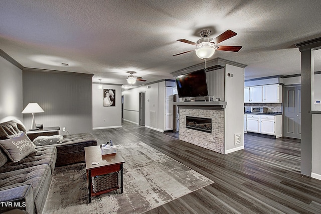 living area with dark wood-type flooring, ornamental molding, a ceiling fan, a textured ceiling, and a fireplace