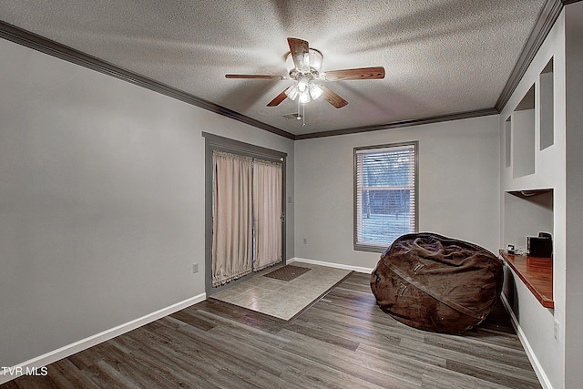 interior space featuring a textured ceiling, wood finished floors, baseboards, and ornamental molding