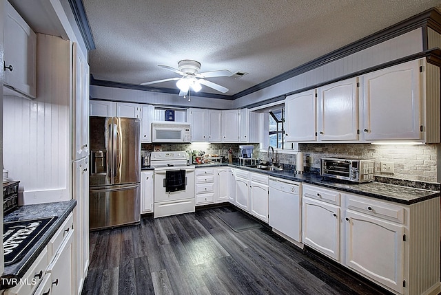 kitchen with dark countertops, dark wood finished floors, ornamental molding, white appliances, and a sink