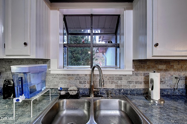 kitchen featuring backsplash, white cabinets, dark stone counters, and a sink