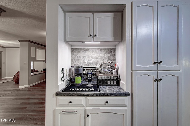 kitchen with dark countertops, decorative backsplash, wood finished floors, white cabinets, and a textured ceiling