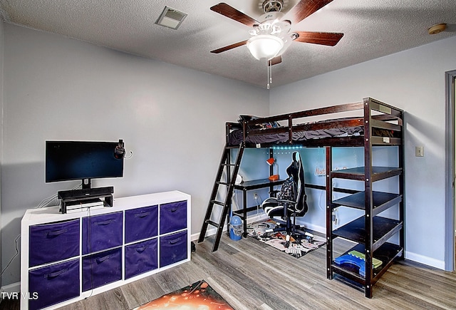 bedroom with visible vents, a ceiling fan, a textured ceiling, wood finished floors, and baseboards