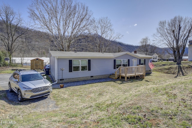 view of front of property with a deck with mountain view, crawl space, an outdoor structure, and a front yard