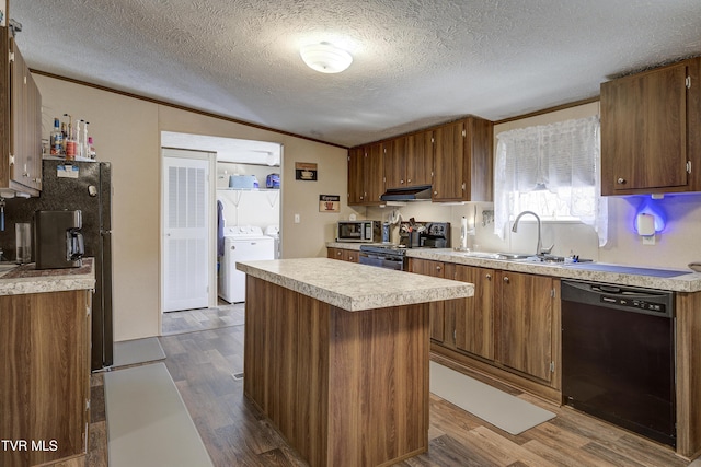 kitchen with dark wood-style floors, light countertops, black appliances, washing machine and dryer, and a sink