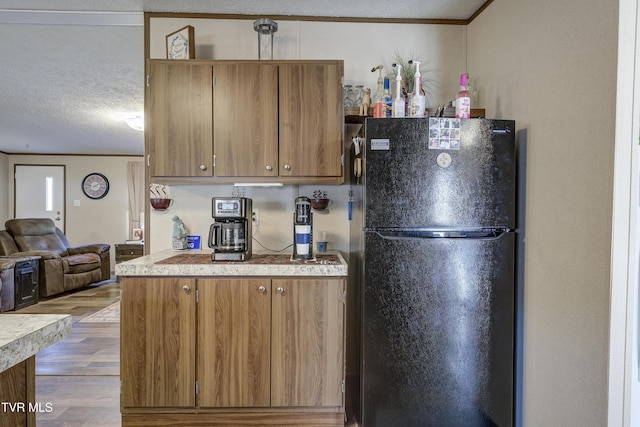 kitchen with a textured ceiling, wood finished floors, light countertops, freestanding refrigerator, and crown molding