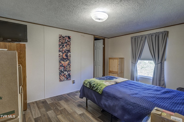 bedroom with ornamental molding, freestanding refrigerator, a textured ceiling, and wood finished floors