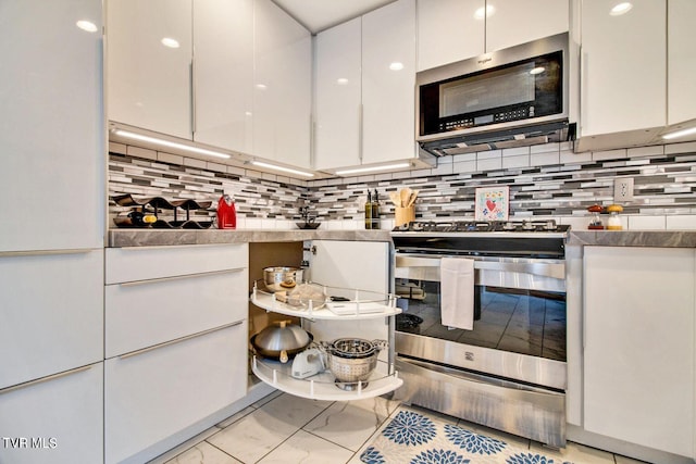 kitchen featuring white cabinets, marble finish floor, appliances with stainless steel finishes, and decorative backsplash