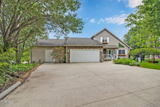 traditional home with an attached garage, stone siding, driveway, and fence