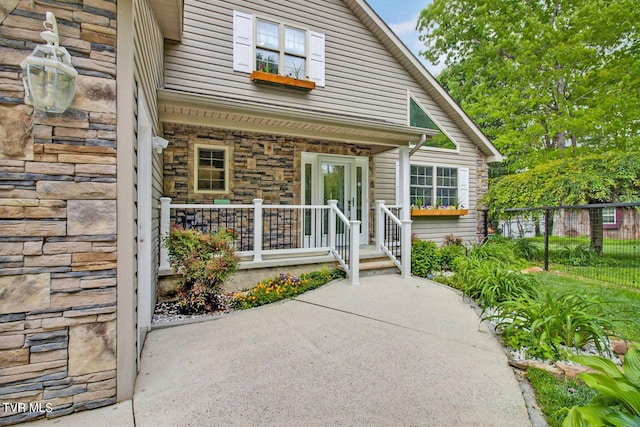 doorway to property featuring stone siding, a porch, and fence