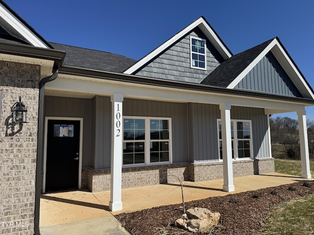 doorway to property with roof with shingles, a porch, board and batten siding, and brick siding