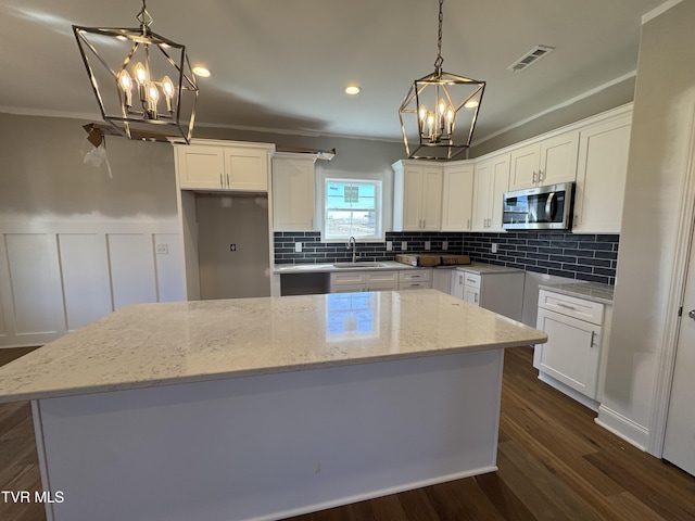 kitchen featuring stainless steel microwave, a kitchen island, a sink, and a notable chandelier