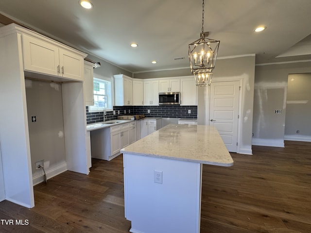 kitchen featuring a kitchen island, white cabinets, decorative backsplash, stainless steel microwave, and dark wood finished floors