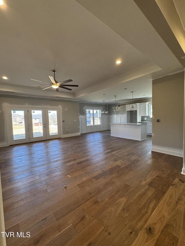 unfurnished living room with baseboards, a tray ceiling, dark wood finished floors, and a ceiling fan