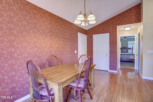 dining room with lofted ceiling, wood finished floors, a chandelier, baseboards, and wallpapered walls