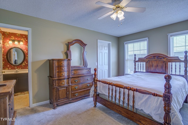 bedroom featuring light colored carpet, ensuite bathroom, a sink, a textured ceiling, and baseboards