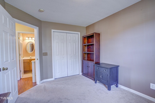 bedroom with a closet, light colored carpet, a textured ceiling, and baseboards