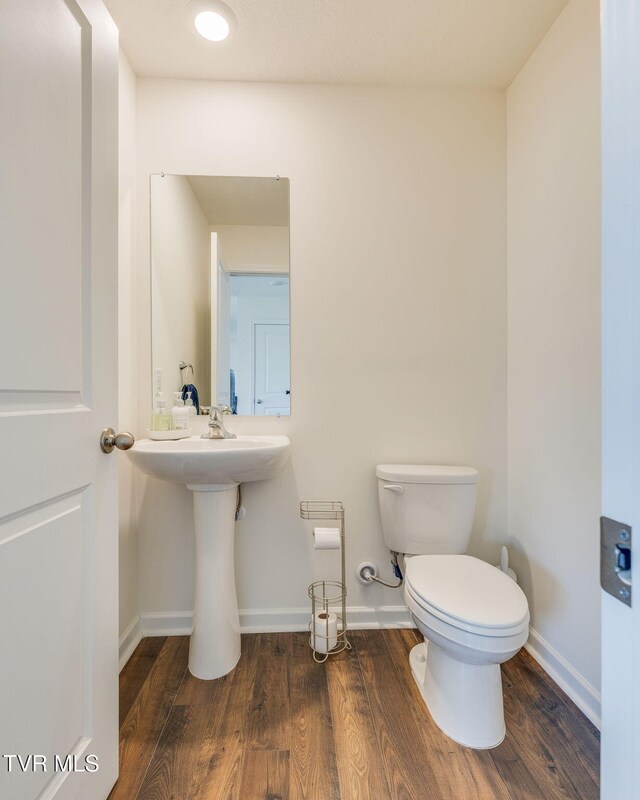 half bathroom with wood finished floors, toilet, and baseboards