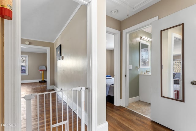 hallway featuring attic access, dark wood-type flooring, crown molding, and baseboards