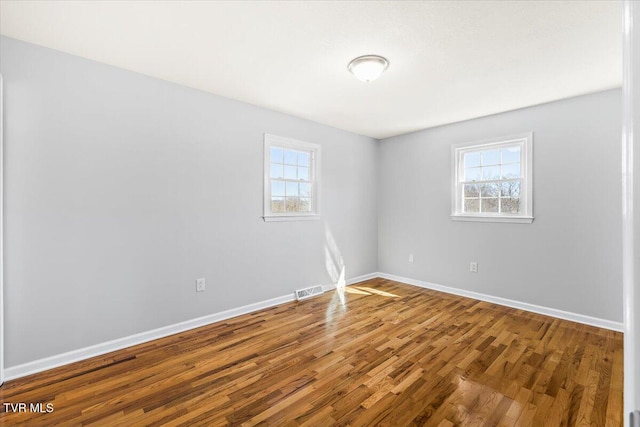 empty room with plenty of natural light, wood finished floors, visible vents, and baseboards